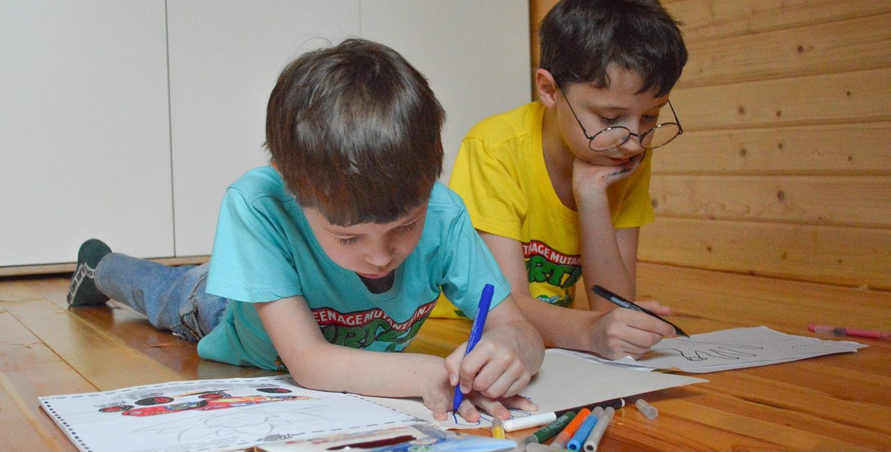 Dos niños tirados en el suelo dibujando